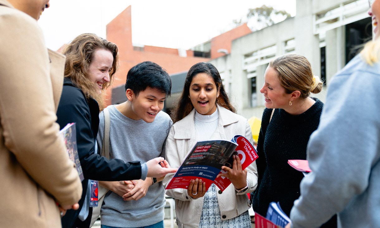 Four students sit on a bench laughing and smiling.